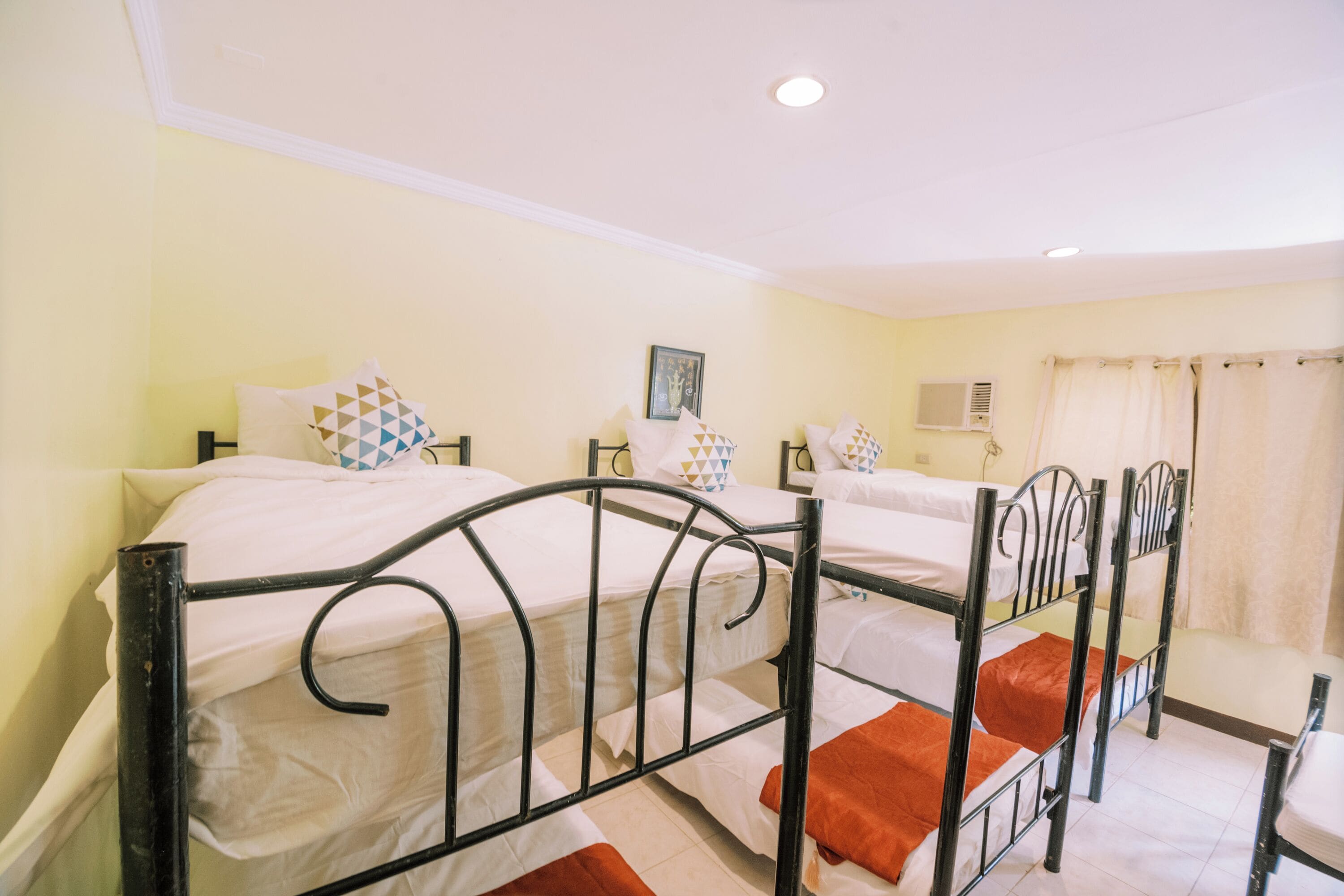 Una habitación con tres literas, una cama individual, una ventana con cortinas y un aire acondicionado instalado en la pared.