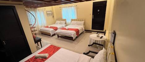 A hotel room with three beds, a small table, and a wall-mounted TV.
