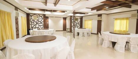 A spacious banquet hall with multiple round tables covered with white tablecloths and chairs.