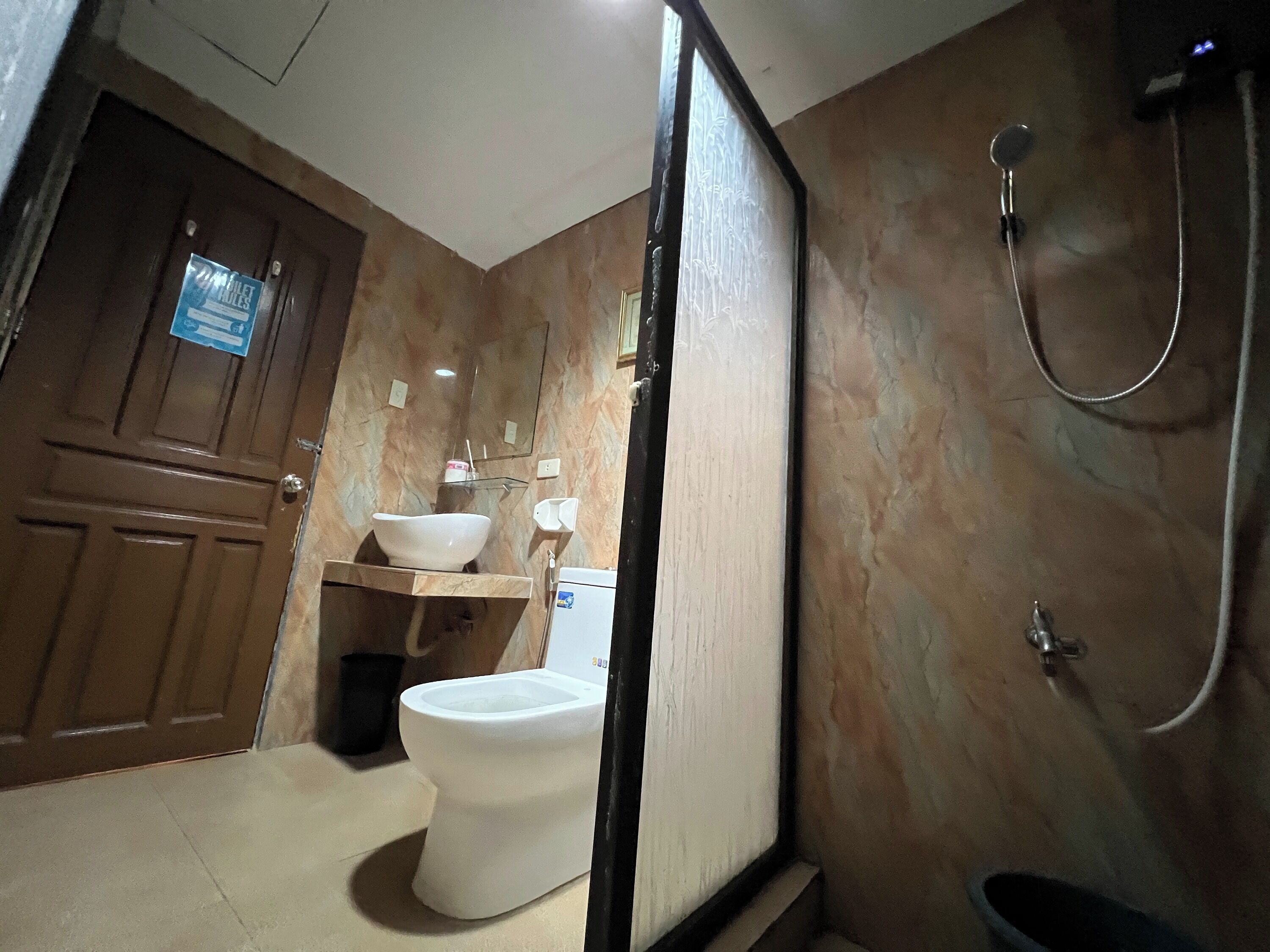 A bathroom with a marble wall, a wooden door, a white sink, a toilet, and a shower.