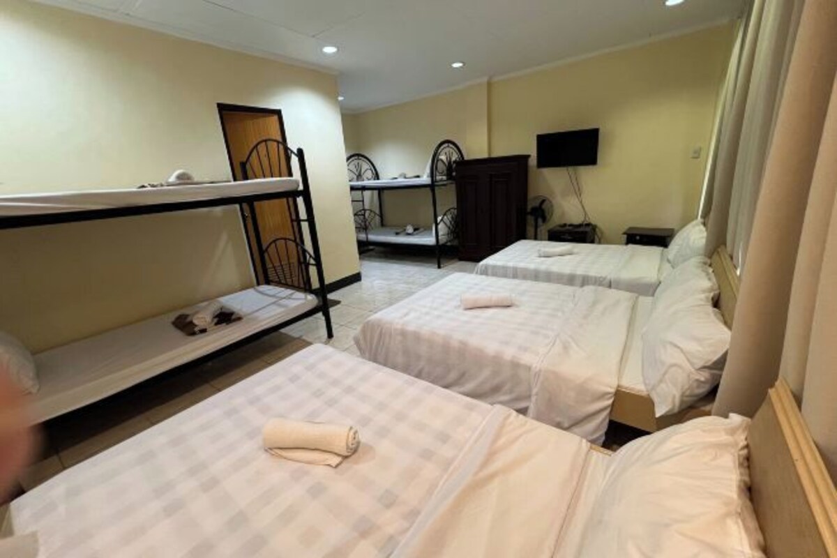 Quarto de hotel com beliches, uma cama de solteiro, televisão e escrivaninha.
