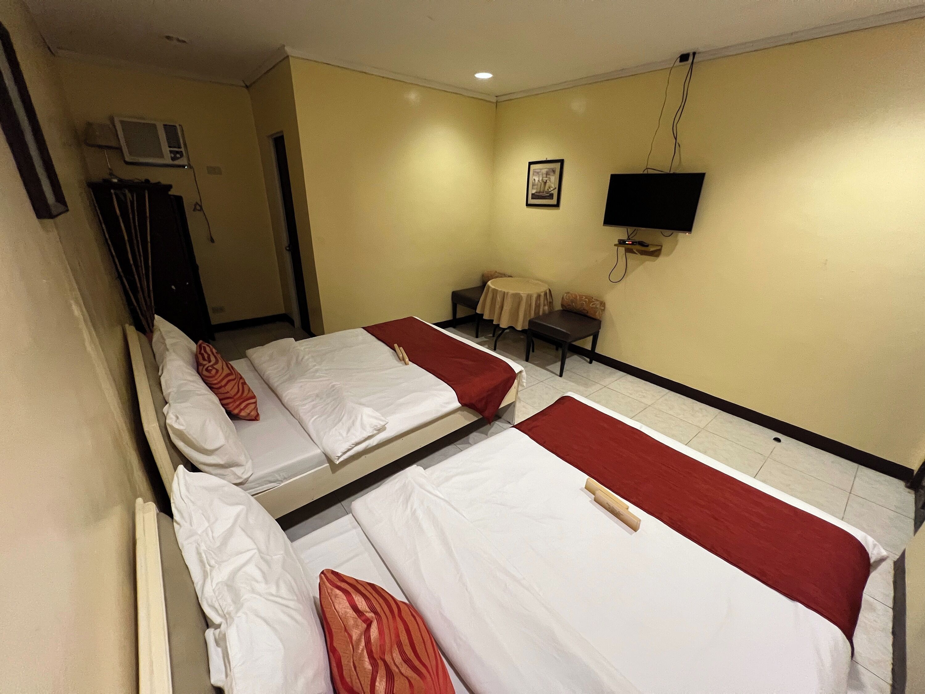 A hotel room with three beds, a TV mounted on the wall, and a small table with a chair.