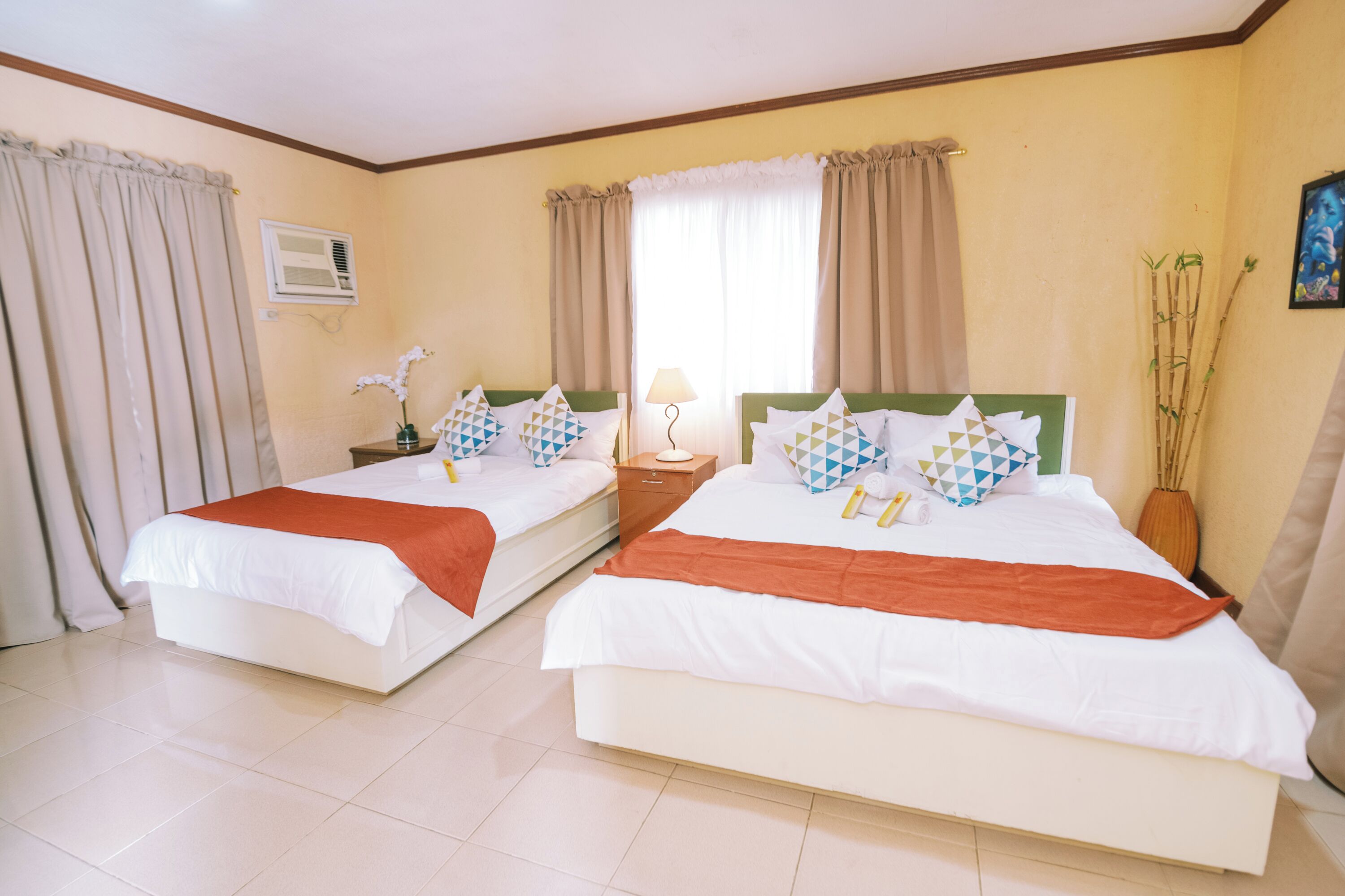 Une chambre d’hôtel avec deux lits, une fenêtre avec des rideaux, une table de chevet avec une lampe et un climatiseur fixé au mur.