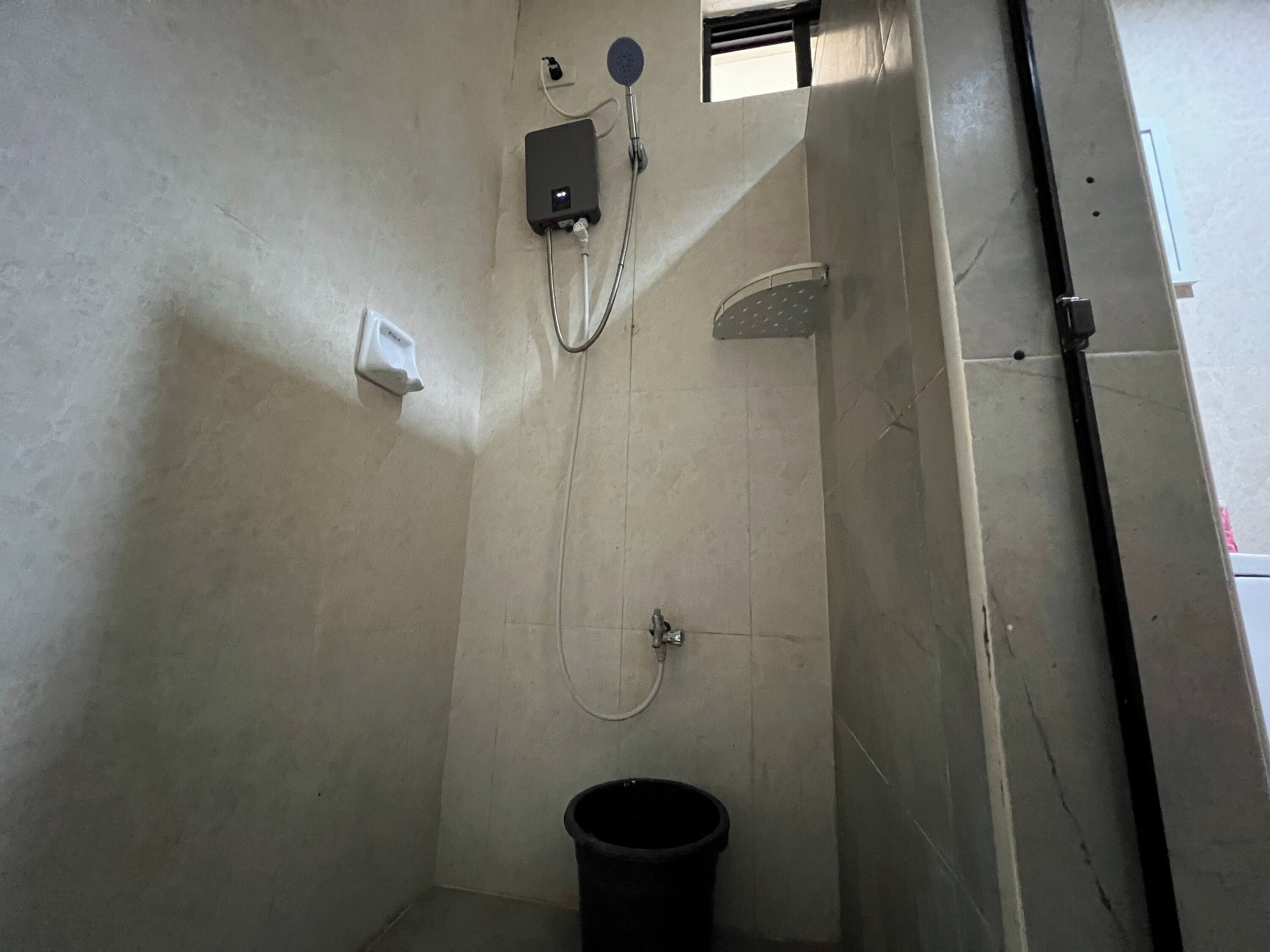 A small, utilitarian bathroom with a shower, a hand dryer, and a trash bin.