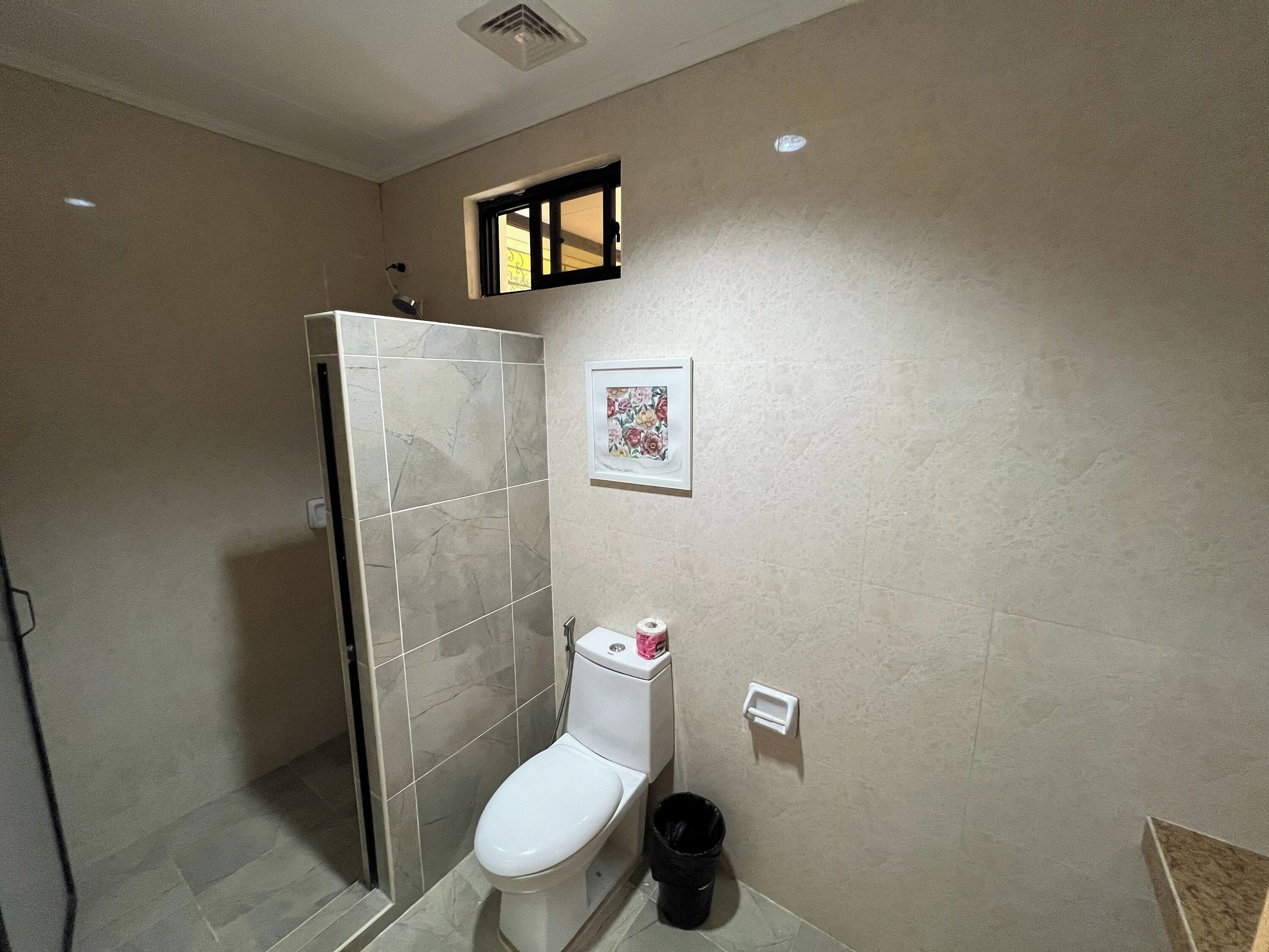 A bathroom with a toilet, a shower, and a small trash bin.