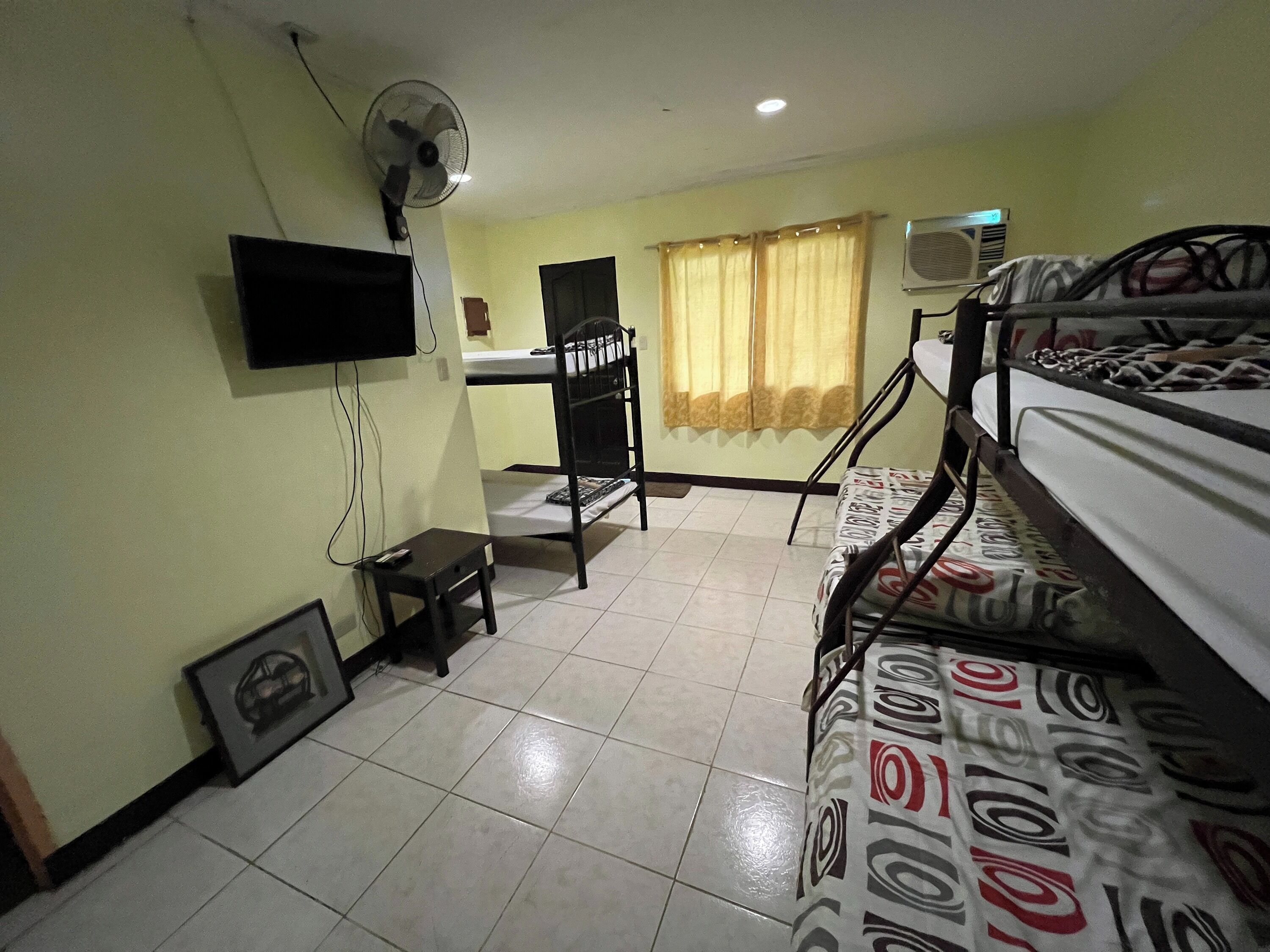 A room with bunk beds, a desk, a chair, a TV, and an air conditioning unit.