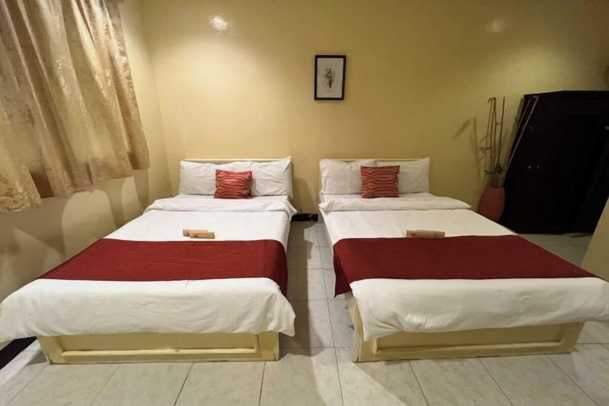 A room with two beds, each with a red blanket and white bedding.
