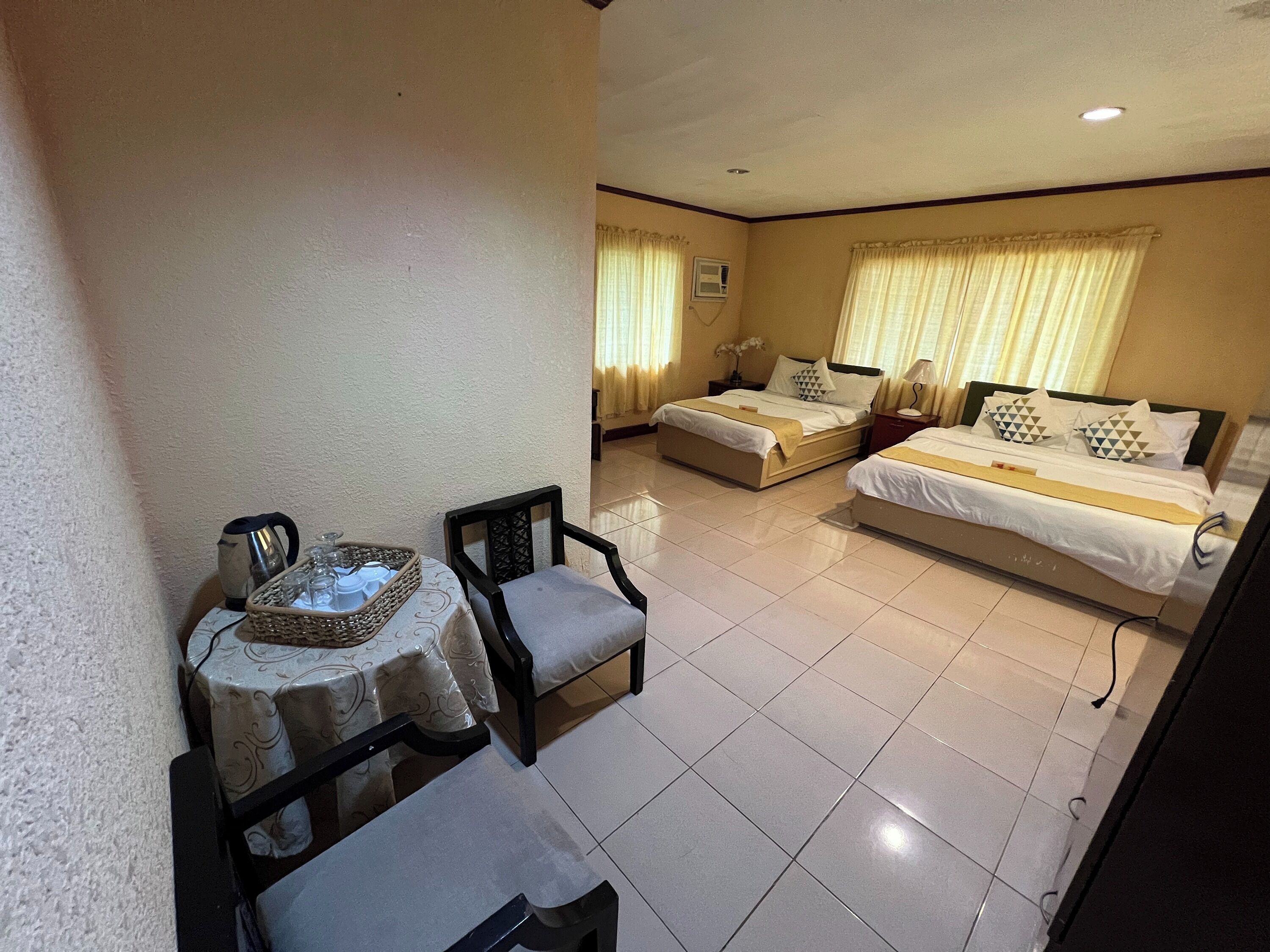 A hotel room with two beds, a small table with a tray of glasses, and a chair.