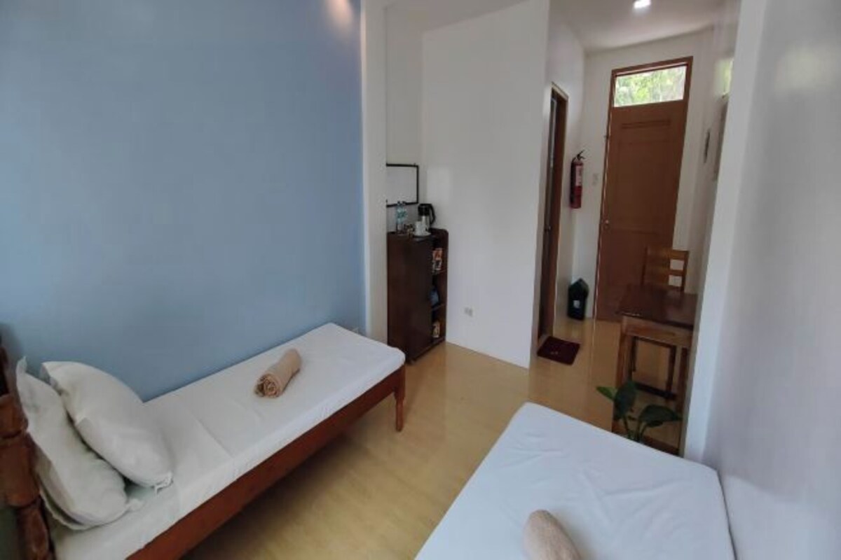 Una habitación con dos camas individuales, un armario de madera, una mesita y una puerta que da a otra estancia.