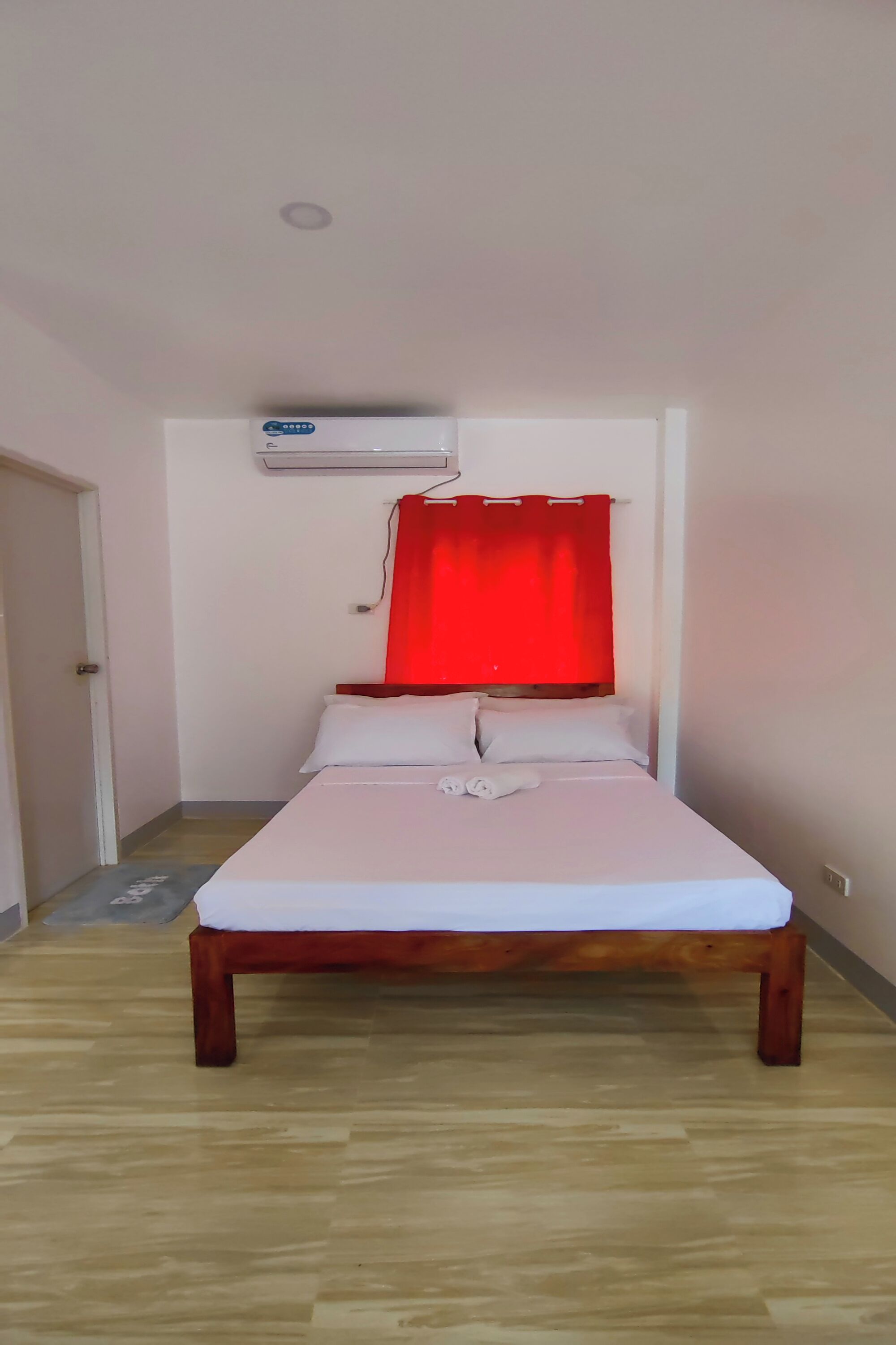 Un lit simple avec un cadre en bois, du linge de lit blanc et un rideau rouge.