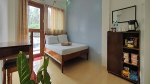 Een slaapkamer met een bed, een houten bureau, een kast met etenswaren en een raam met gordijnen.