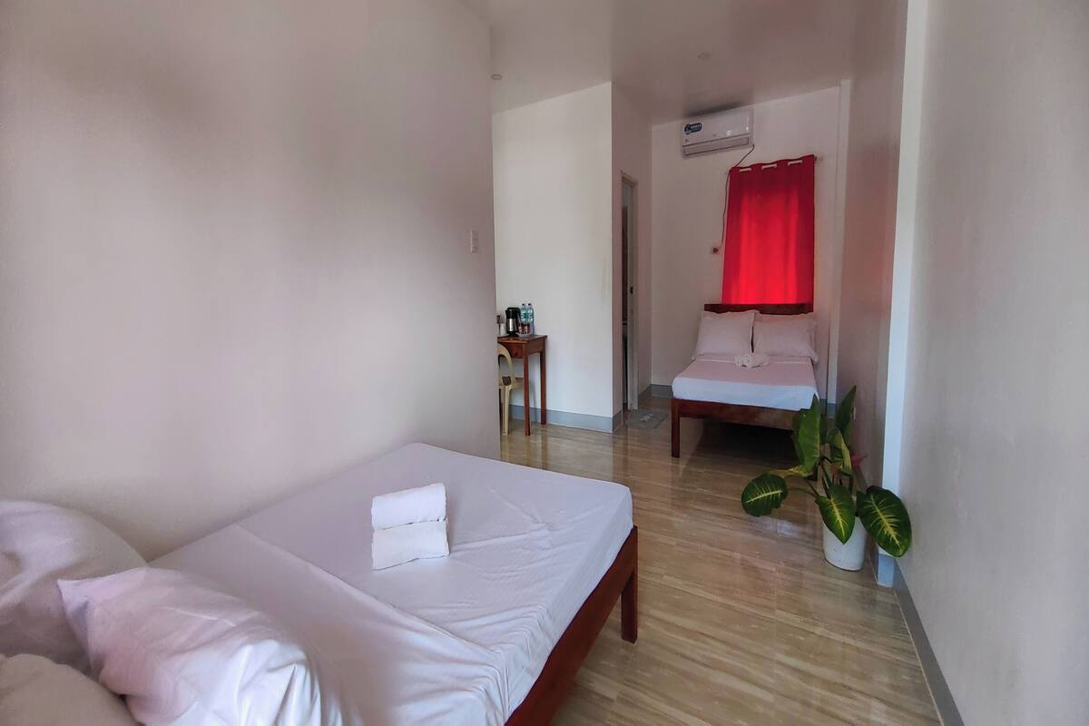 Une chambre d’hôtel avec un lit, une petite table et une chaise, un lavabo et une plante en pot.