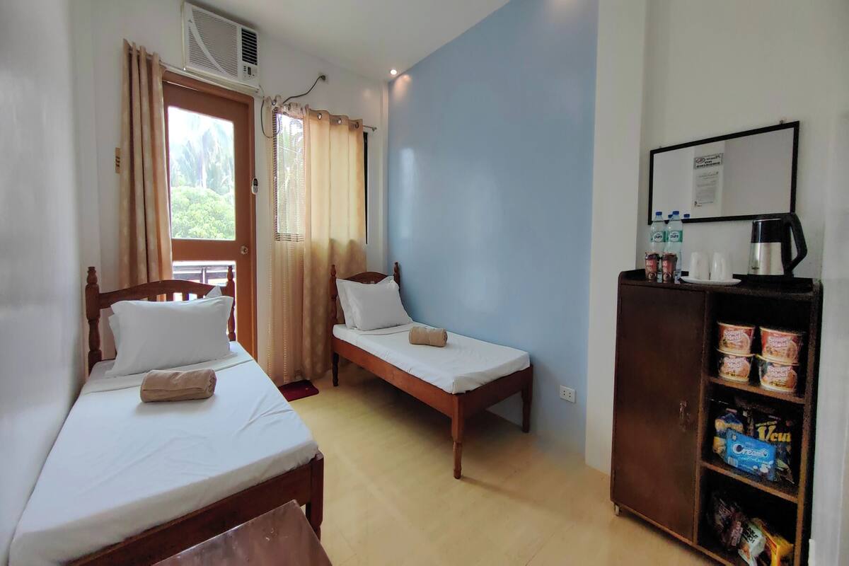 Une chambre avec deux lits simples, un meuble en bois contenant des collations, une machine à café et une fenêtre avec des rideaux.