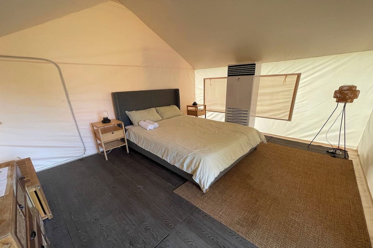 A tented bedroom with a bed, bedside table, lamp, and a view of the outside.