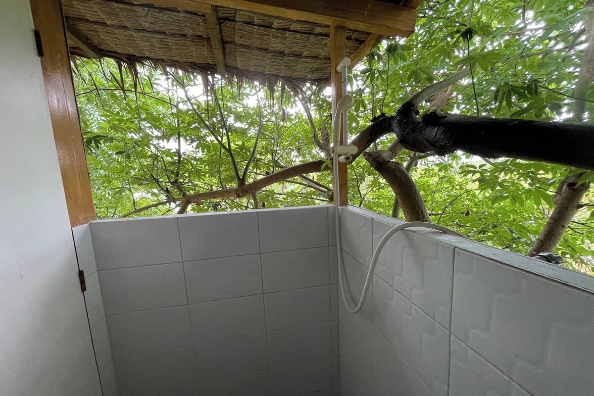 A shower area with tiled walls and a view of a tree outside.