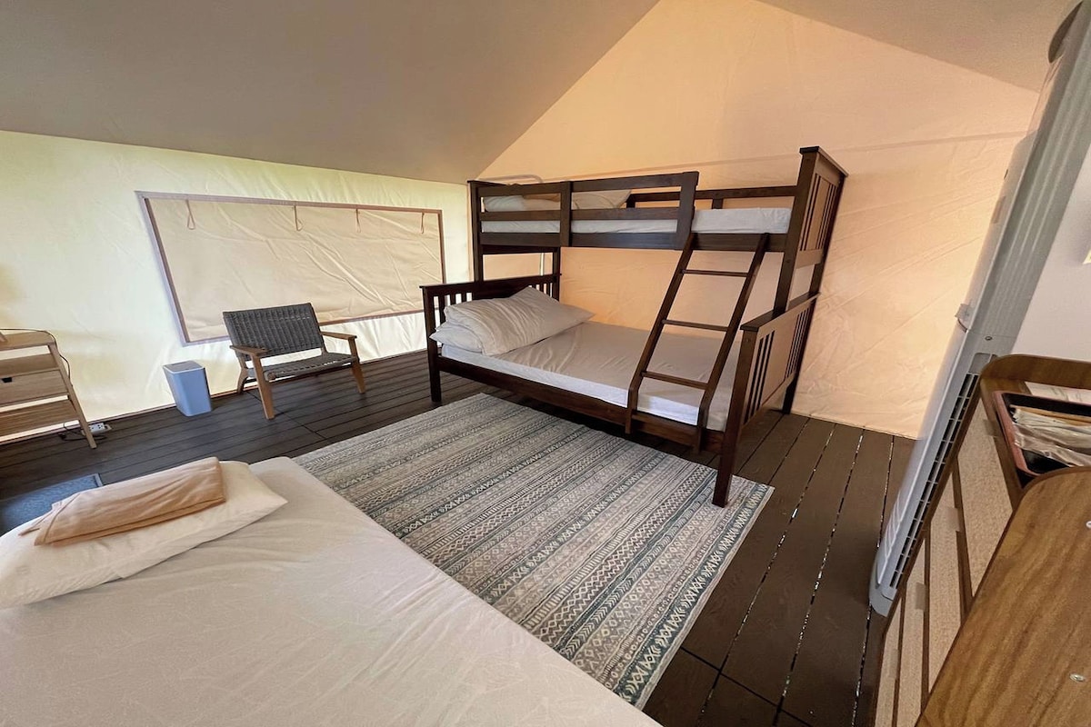 Una habitación con carpa, una cama litera, una silla, un escritorio y una mesita.