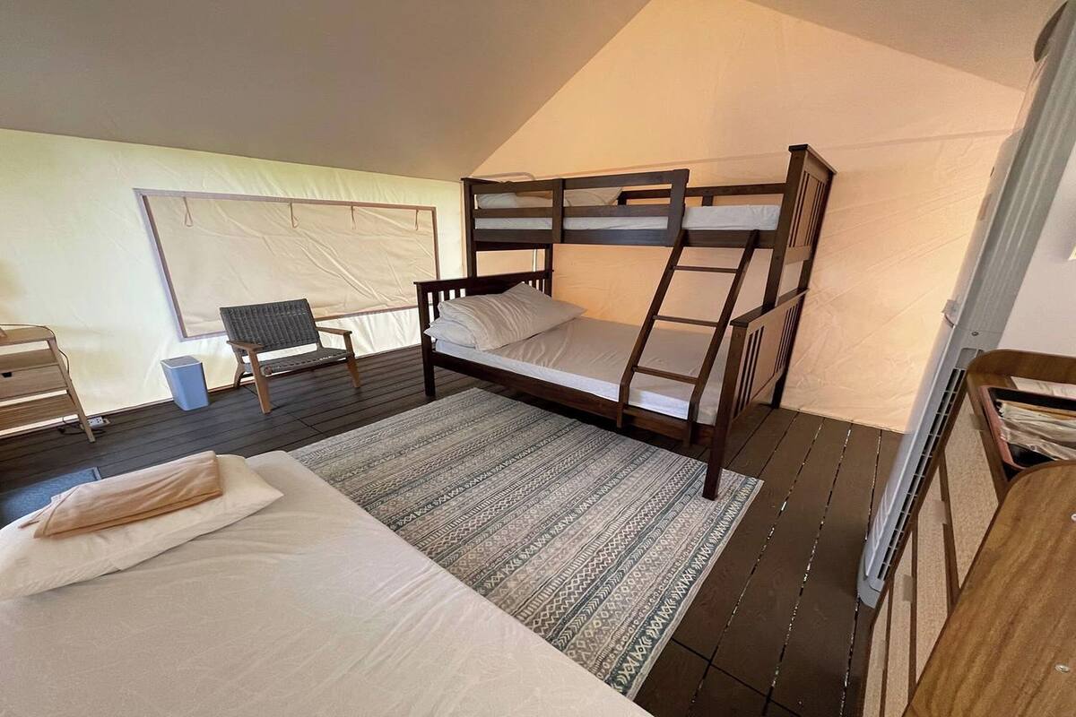 A tented room with a bunk bed, a chair, a desk, and a small table.