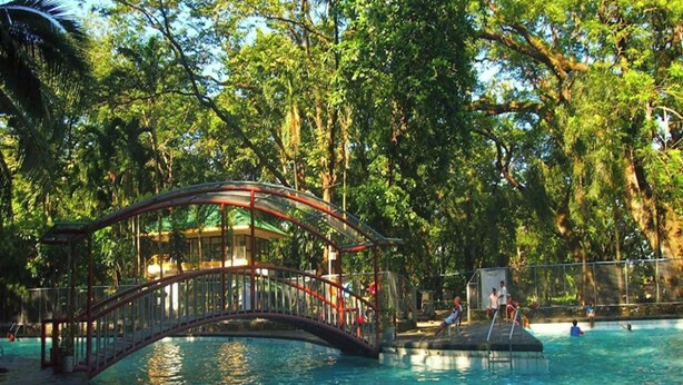 A swimming pool with a bridge, surrounded by trees. - Santillana Hillside Farms (Arayat)