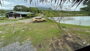 A yellow SUV parked in front of a building with a green roof, near a body of water and a dock. - Santillana Hillside Farms (Arayat)
