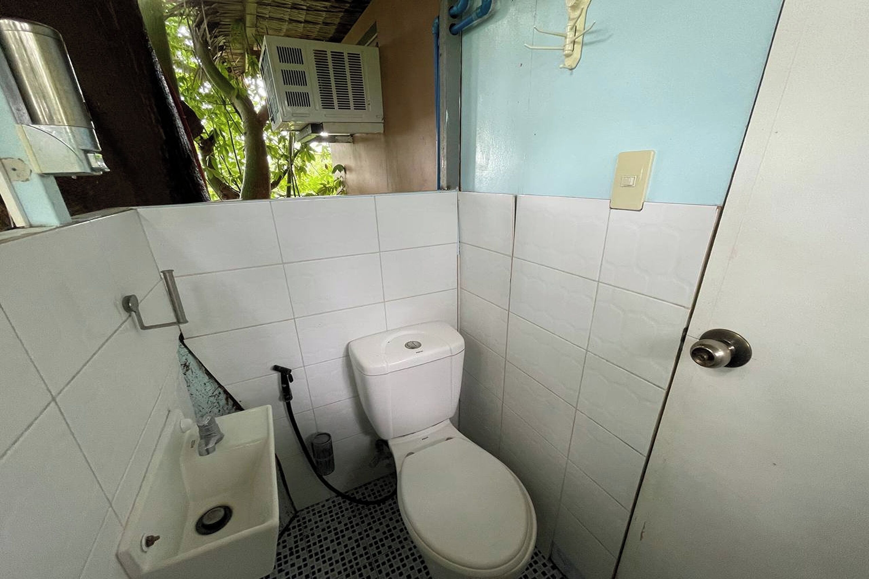 Une petite salle de bain carrelée, équipée de toilettes, d’un lavabo et d ’un espace douche.