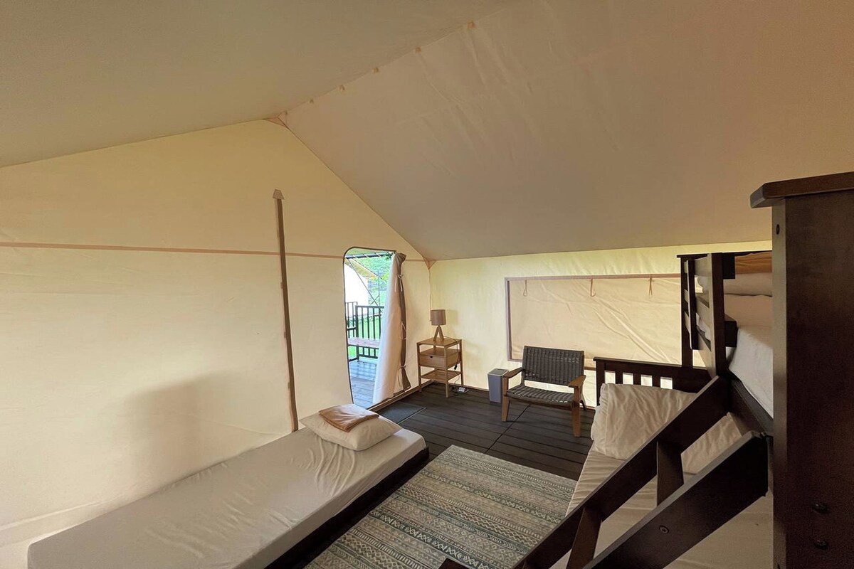 A tented accommodation with two beds, a small table, and a chair.
