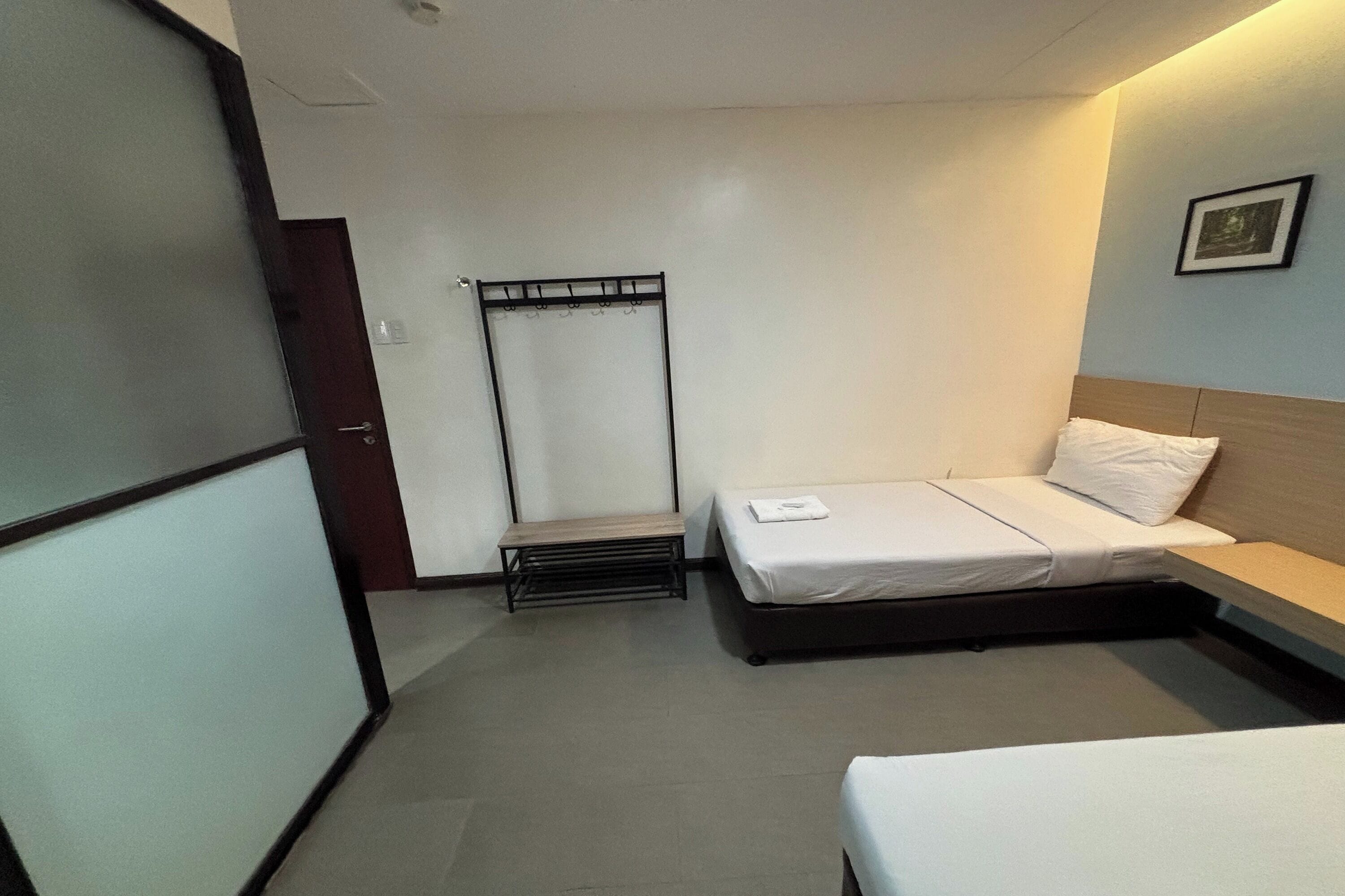 Habitación de hotel con una cama individual, un banco y un perchero.