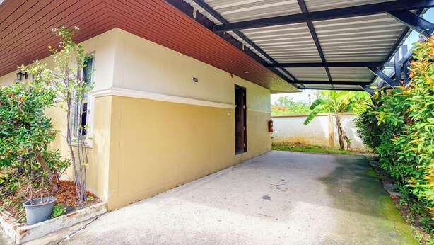 Un espace extérieur abrité, doté d’un sol en béton, d’un plafond en bois et d’un mur de couleur beige.