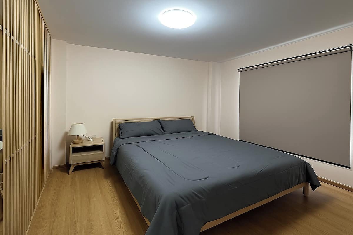 Une chambre à coucher avec un lit, une table de chevet, une lampe et une fenêtre avec un store.