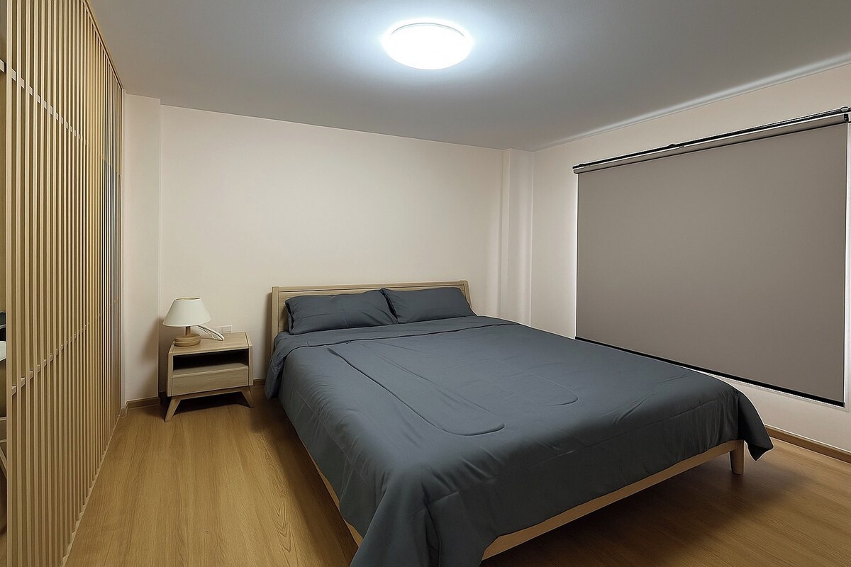 Un dormitorio con cama, mesita de noche, lámpara y ventana con persiana.
