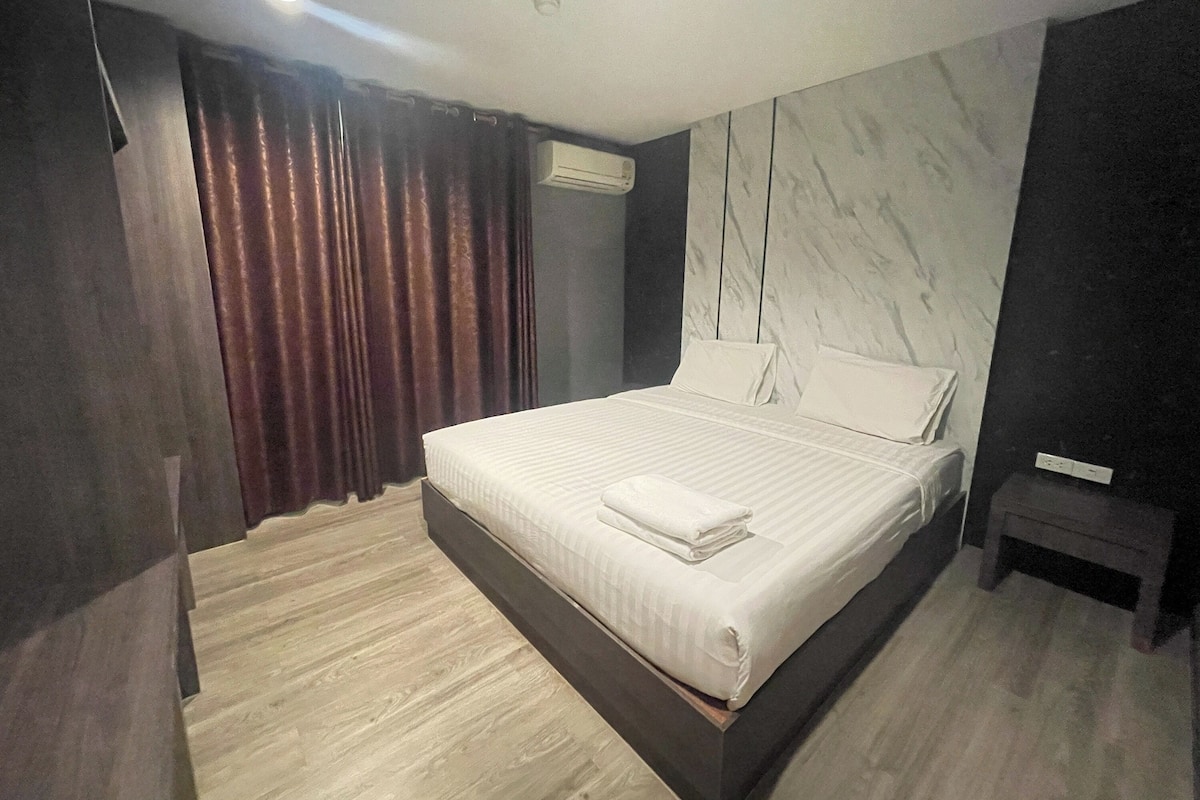 A modern bedroom with a large bed, dark curtains, a marble wall, and a wooden floor.