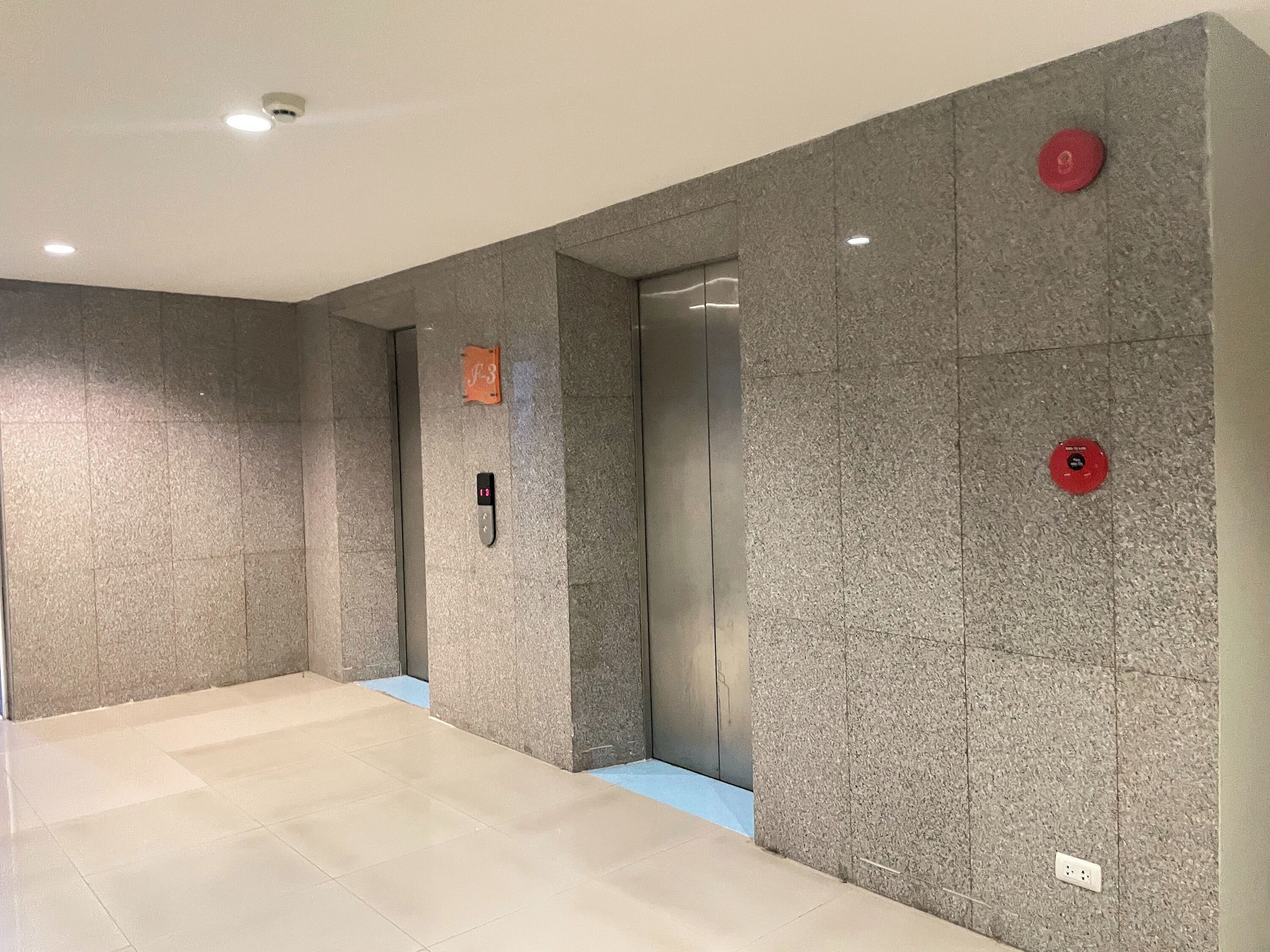 A modern elevator with a digital display, a fire alarm button, and a maintenance label on the wall.