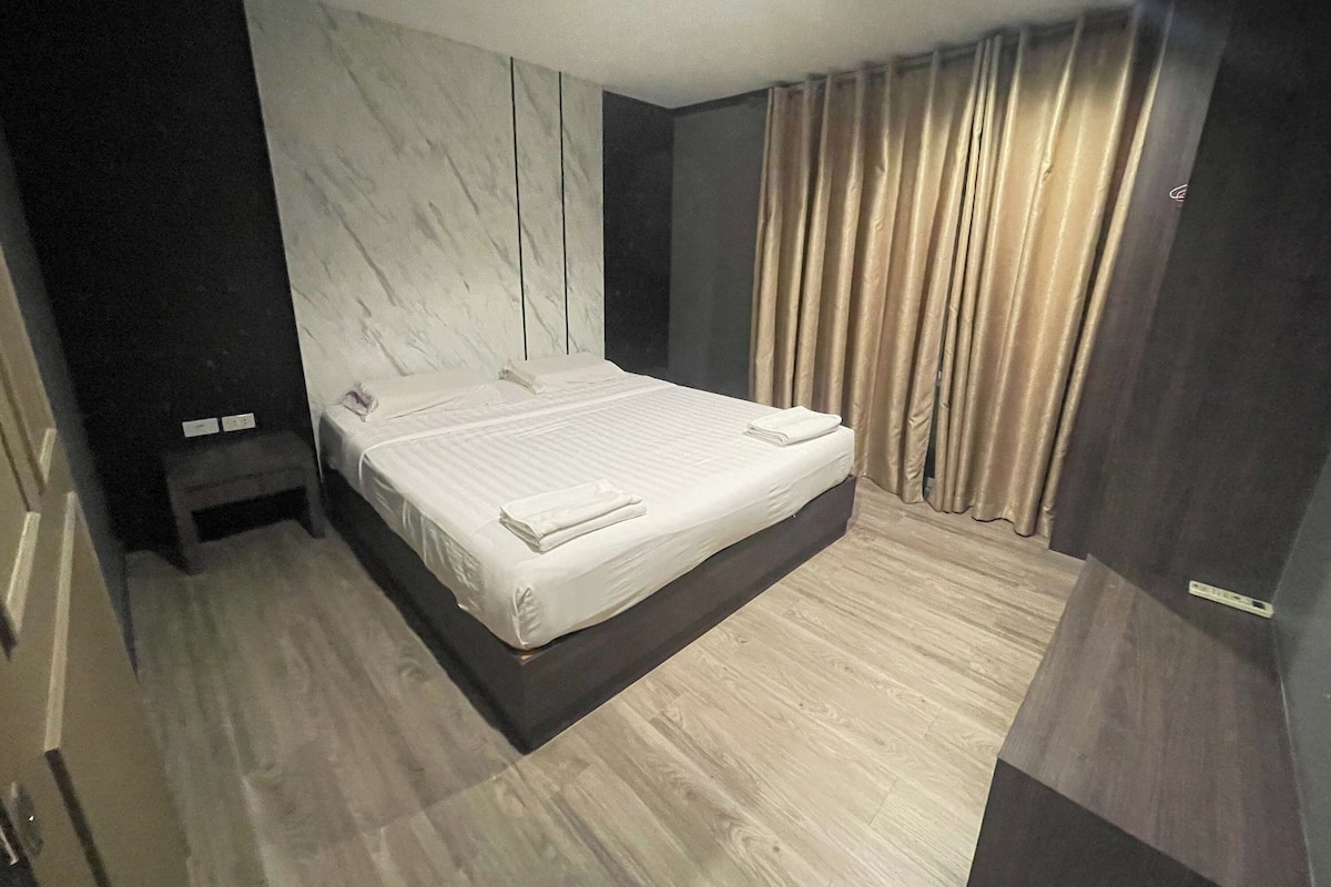 A modern bedroom with a large bed, dark walls, and a wooden floor.