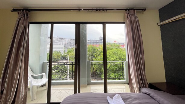 Een hotelkamer met een bed, een balkon met een stoel en uitzicht op gebouwen en groen.