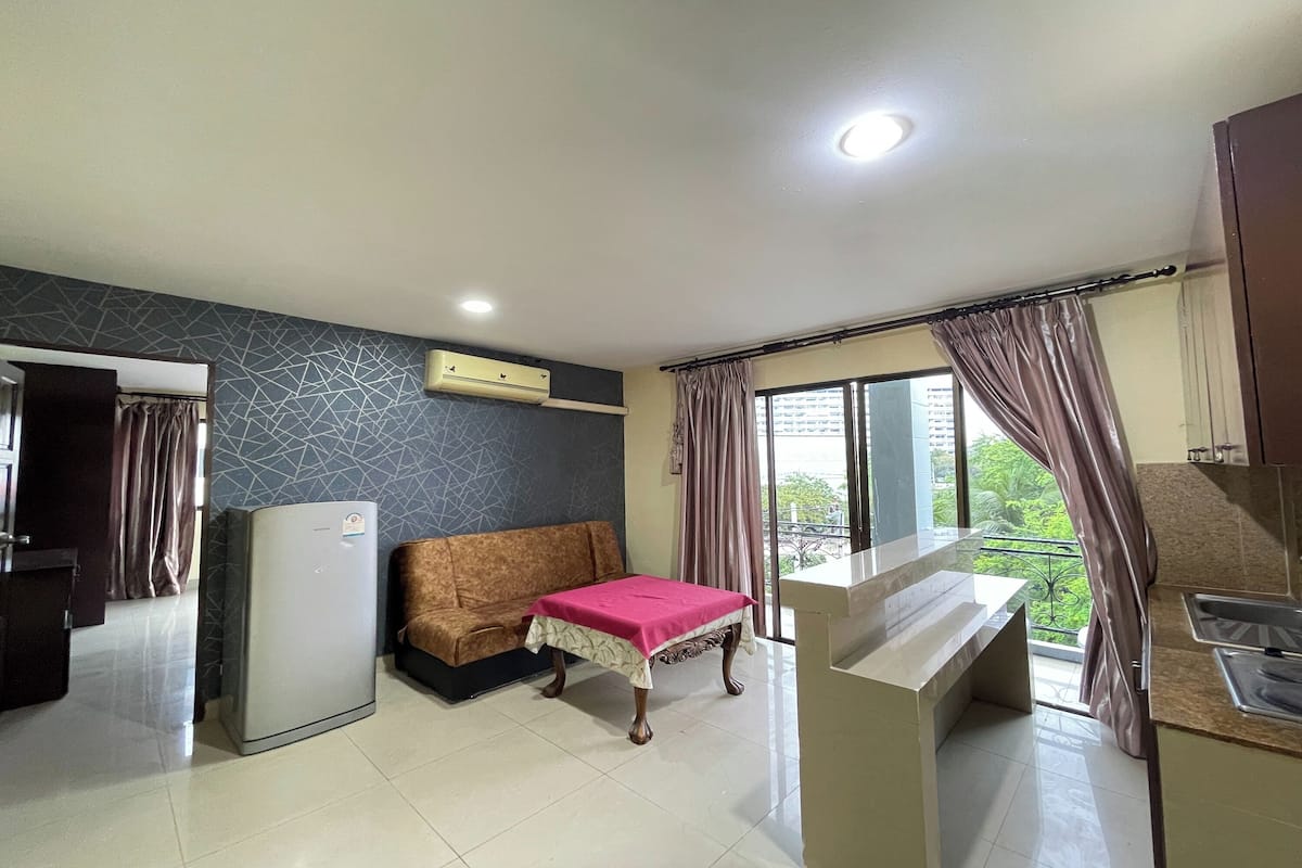 A compact living space with a kitchenette, a sofa, a small table, and a window with curtains.