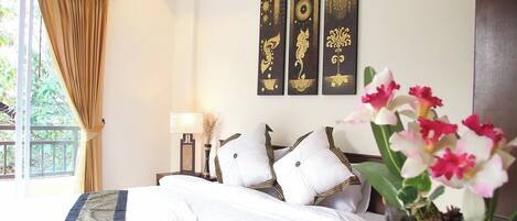 A hotel room with a bed, a nightstand, a lamp, and a window with curtains. There are three wall-mounted paintings above the bed.