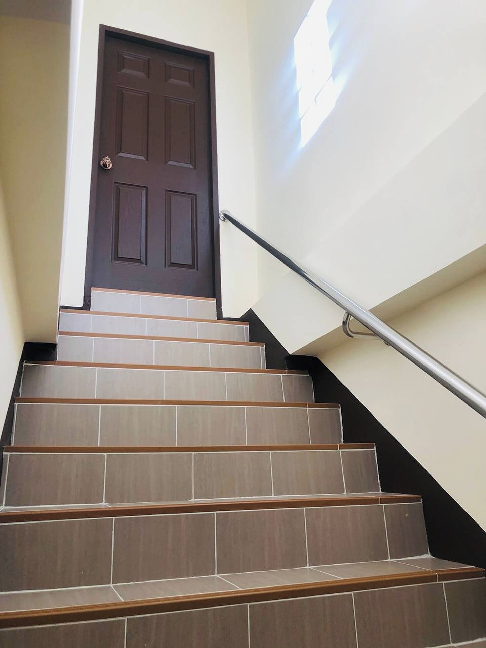 Una escalera que lleva a un rellano con barandilla metálica, coronada por una puerta de color marrón oscuro.