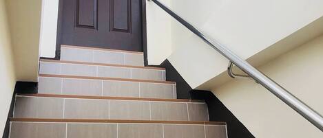 Una escalera que lleva a un rellano con barandilla metálica, coronada por una puerta de color marrón oscuro.