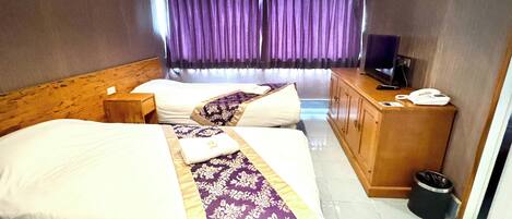 A hotel room with two beds, a wooden headboard, a desk with a telephone, and a window with purple curtains.