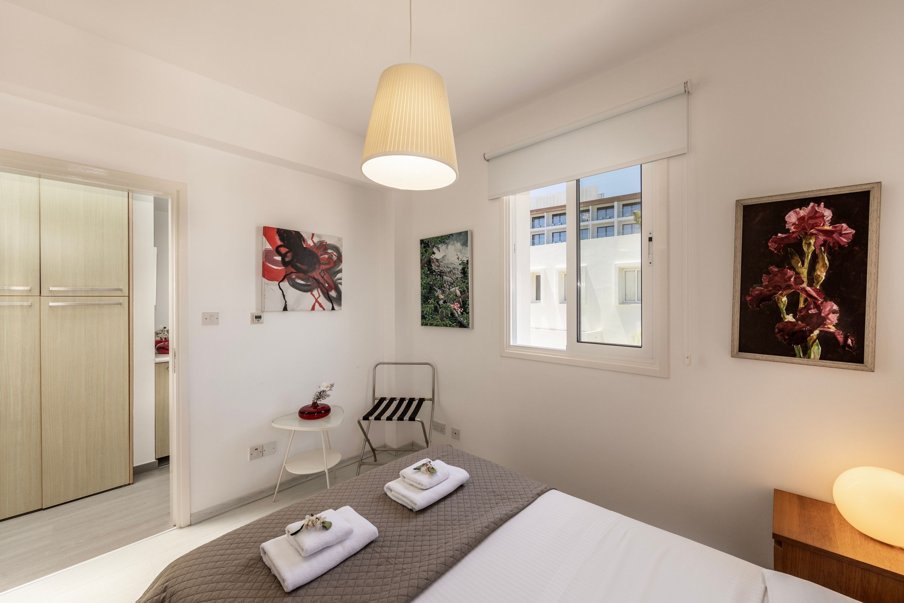 A bedroom with a bed, a chair, a small table, and artwork on the walls.