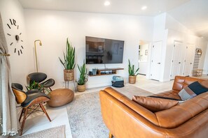 A modern living room with a leather sofa, a flat-screen TV, and a dining area visible through an open door. - Stonecliff Escape Sum (Page)