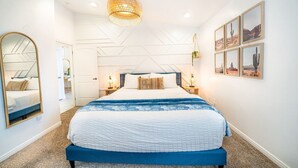 A modern bedroom with a large bed, a hanging light fixture, and framed pictures on the wall.