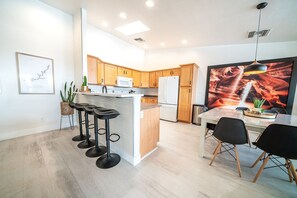 Una cocina moderna con armarios de madera, una isla central, taburetes de bar y un comedor con mesa y sillas.