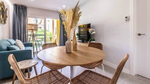 Un salón moderno con una mesa de comedor redonda de madera, sillas de mimbre, un sofá azul y un ventanal con cortinas.
