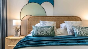 Una cama con cabecera trenzada, varios almohadones y una manta verde azulada.