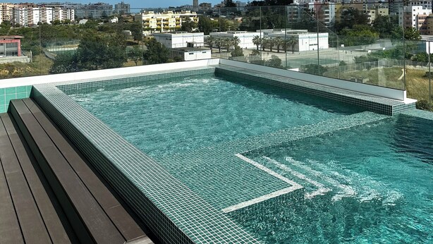 A rooftop pool with clear blue water, surrounded by a wooden deck and a cityscape view. - Lovely Studio (Faro)