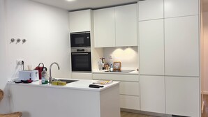 A modern kitchen with white cabinetry, a built-in oven, and a central island with a sink. - Lovely Studio (Faro)