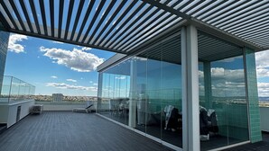 A modern rooftop terrace with a glass enclosure, a metal roof, and a view of the cityscape. - Lovely Studio (Faro)