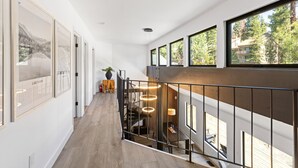 A modern interior with a wooden floor, a staircase with a railing, and large windows offering a view of trees and buildings. - Lake Daze in Kings Beach (Kings Beach)