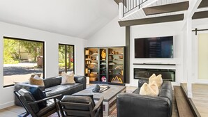 A modern living room with leather sofas, a coffee table, and a fireplace. There is a large TV mounted on the wall and a bookshelf filled with decorative items. - Lake Daze in Kings Beach (Kings Beach)