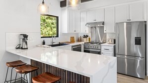 A modern kitchen with white cabinets, stainless steel appliances, a large island with stools, and pendant lighting. - Lake Daze in Kings Beach (Kings Beach)